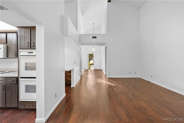 kitchen featuring dark brown cabinetry, white appliances, dark hardwood / wood-style flooring, and a high ceiling