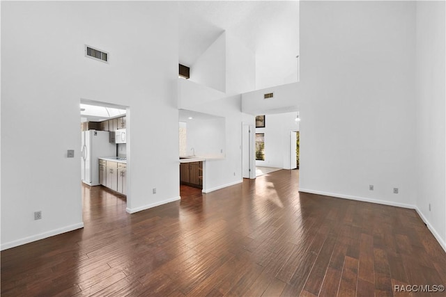 unfurnished living room featuring dark hardwood / wood-style floors, sink, and a high ceiling