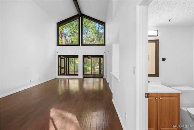 unfurnished living room with beamed ceiling, dark hardwood / wood-style floors, high vaulted ceiling, and a textured ceiling