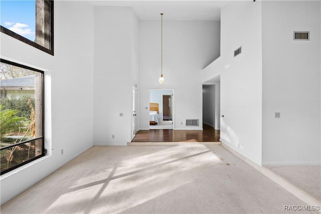 unfurnished living room featuring a towering ceiling, plenty of natural light, and carpet flooring