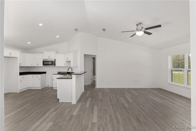 kitchen featuring white cabinets, wood-type flooring, sink, vaulted ceiling, and kitchen peninsula