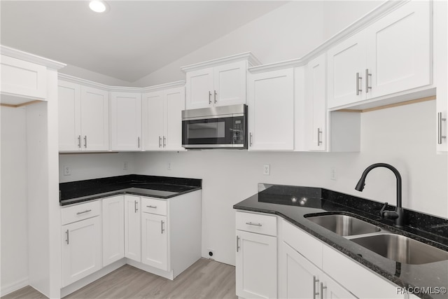 kitchen with white cabinets, sink, vaulted ceiling, dark stone countertops, and light hardwood / wood-style floors