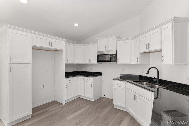 kitchen with white cabinetry, sink, dark stone counters, lofted ceiling, and light wood-type flooring