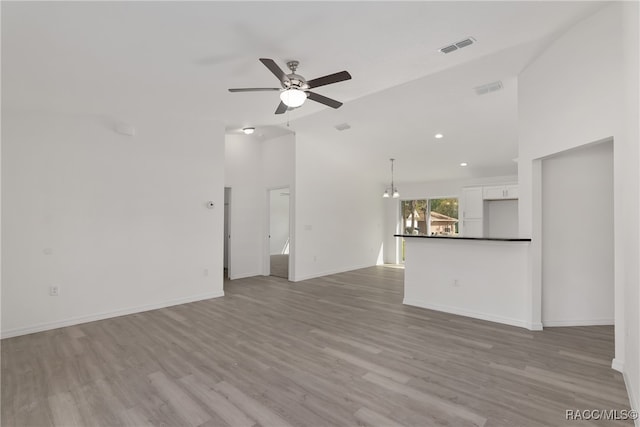 unfurnished living room featuring high vaulted ceiling, light hardwood / wood-style floors, and ceiling fan with notable chandelier