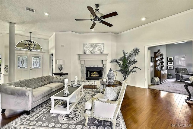 living room with a fireplace, hardwood / wood-style flooring, a textured ceiling, crown molding, and ceiling fan with notable chandelier