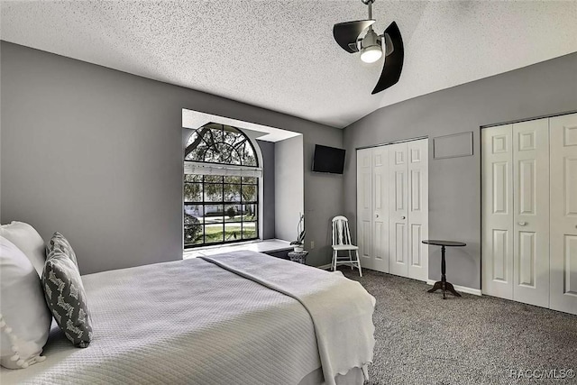 carpeted bedroom with two closets, a ceiling fan, a textured ceiling, baseboards, and vaulted ceiling