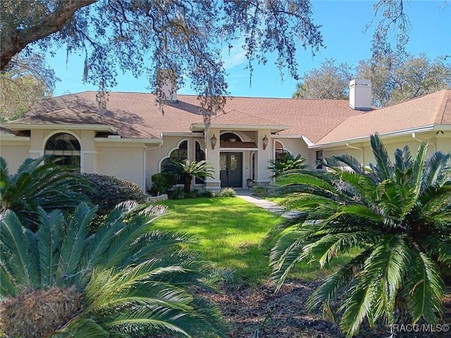 view of front facade with a front yard, a chimney, and stucco siding