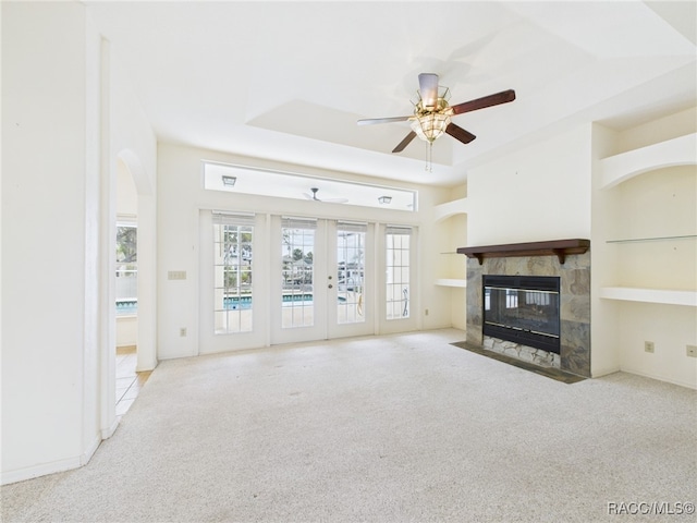 unfurnished living room with french doors, carpet flooring, ceiling fan, and a tiled fireplace