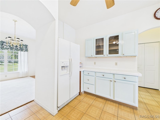 kitchen with glass insert cabinets, white refrigerator with ice dispenser, tile countertops, arched walkways, and ceiling fan with notable chandelier