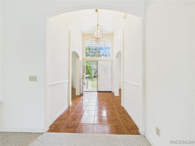tiled entryway with arched walkways, baseboards, and a chandelier