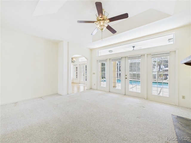 unfurnished living room with carpet floors, a ceiling fan, french doors, and arched walkways