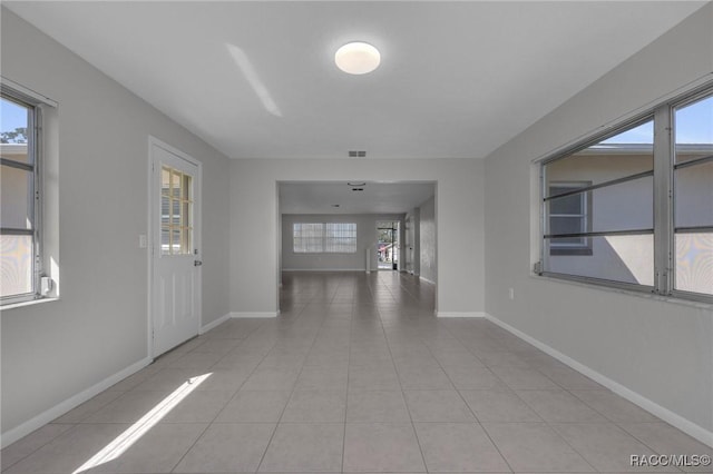 hall with light tile patterned flooring, a healthy amount of sunlight, and baseboards