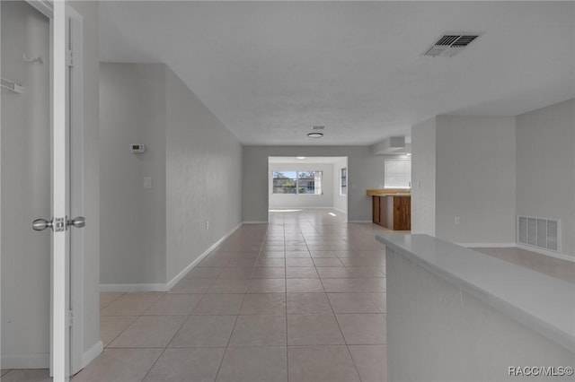 hall with light tile patterned floors, visible vents, and baseboards