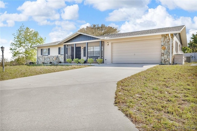 ranch-style house with driveway, an attached garage, a front lawn, stone siding, and central air condition unit