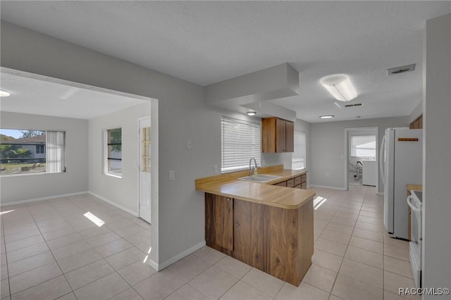 kitchen featuring white appliances, light tile patterned floors, a peninsula, a sink, and light countertops