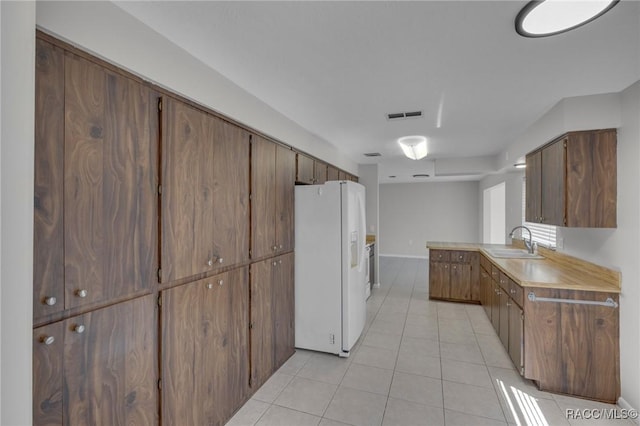 kitchen with light tile patterned floors, visible vents, a sink, light countertops, and white refrigerator with ice dispenser