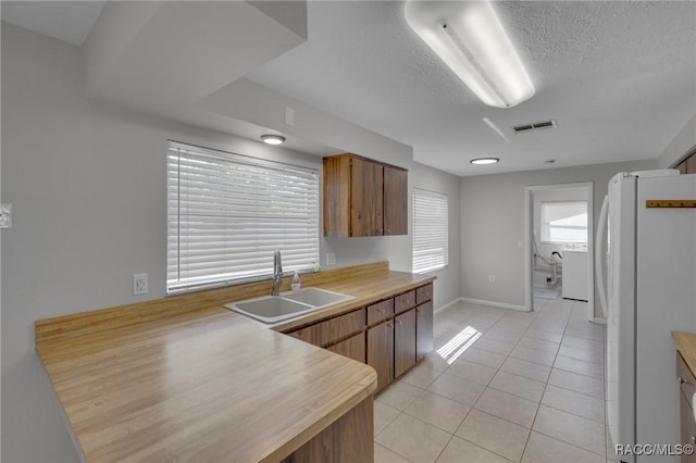 kitchen with visible vents, light countertops, light tile patterned floors, freestanding refrigerator, and a sink