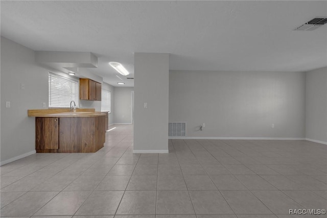 unfurnished living room with light tile patterned flooring, baseboards, visible vents, and a sink