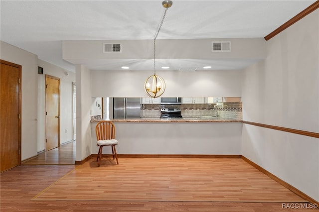 kitchen featuring pendant lighting, backsplash, appliances with stainless steel finishes, light hardwood / wood-style floors, and kitchen peninsula