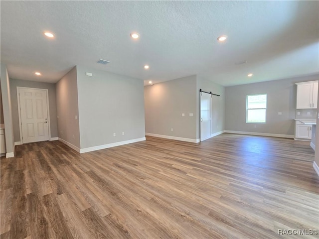 8 Calendula Ct, Homosassa, FL 34446 - unfurnished living room featuring baseboards, a barn door, light wood-type flooring, recessed lighting, and a textured ceiling