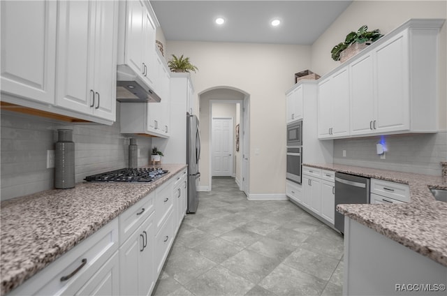 kitchen with light stone countertops, appliances with stainless steel finishes, tasteful backsplash, and white cabinetry