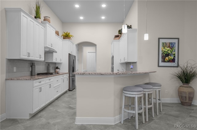 kitchen with light stone counters, kitchen peninsula, a breakfast bar area, white cabinets, and appliances with stainless steel finishes