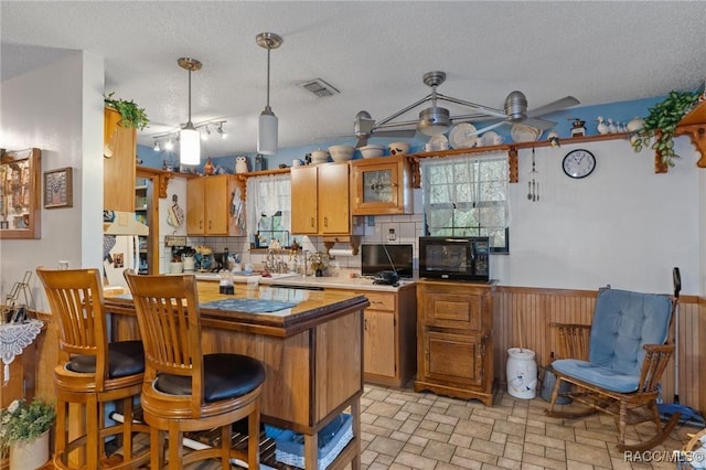 kitchen with ceiling fan, kitchen peninsula, a textured ceiling, a kitchen bar, and wooden walls