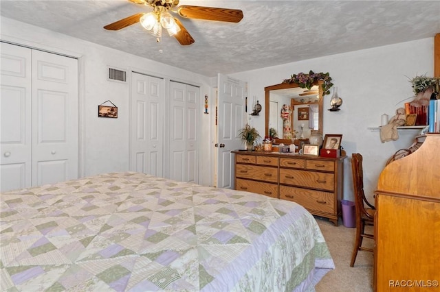 carpeted bedroom with ceiling fan, a textured ceiling, and two closets