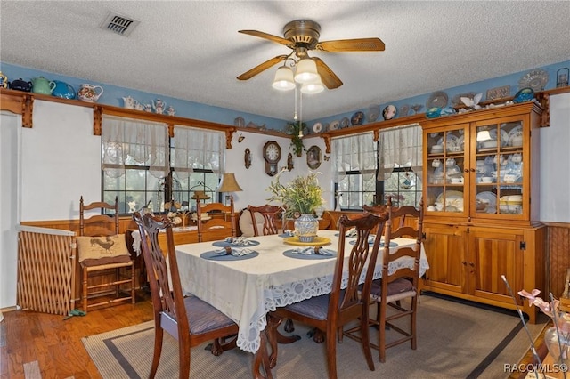 dining space featuring hardwood / wood-style floors, ceiling fan, wood walls, and a textured ceiling