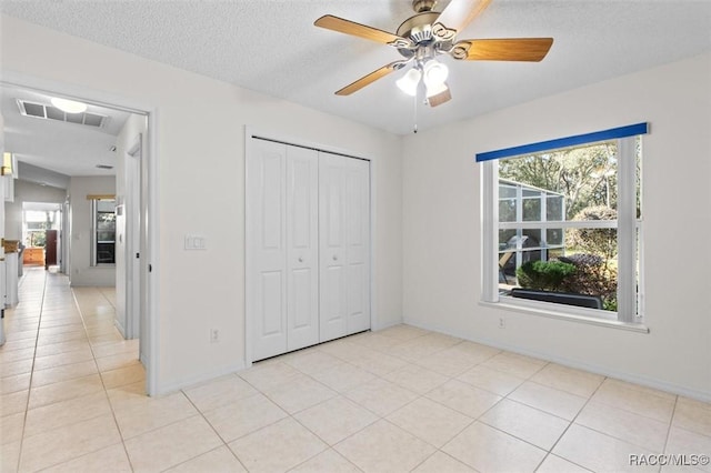 unfurnished bedroom featuring ceiling fan, light tile patterned floors, a closet, and a textured ceiling