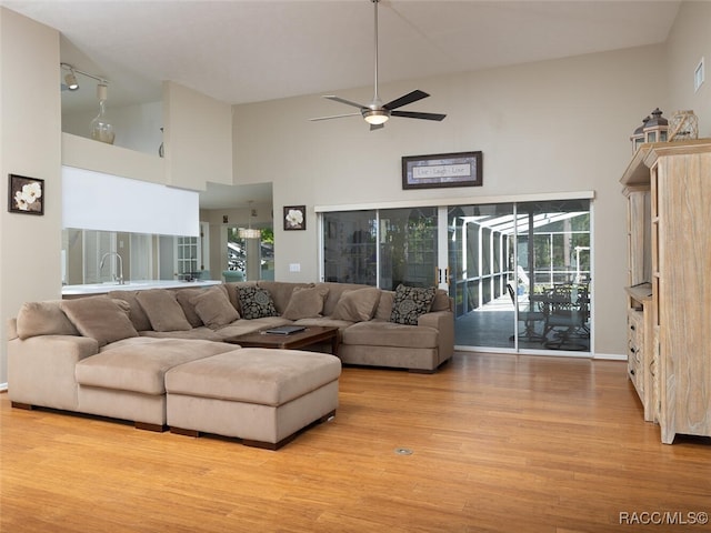 living room with a wealth of natural light, light hardwood / wood-style flooring, high vaulted ceiling, and ceiling fan