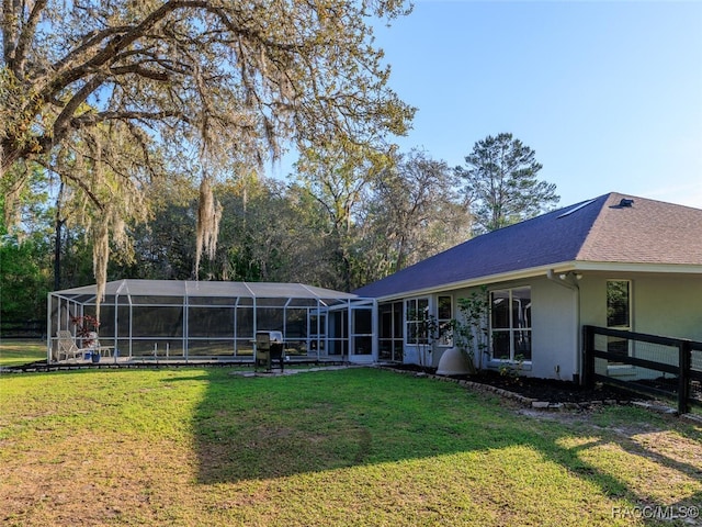 rear view of house with glass enclosure and a yard