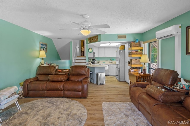 living room featuring a wall mounted air conditioner, a textured ceiling, ceiling fan, sink, and light hardwood / wood-style floors