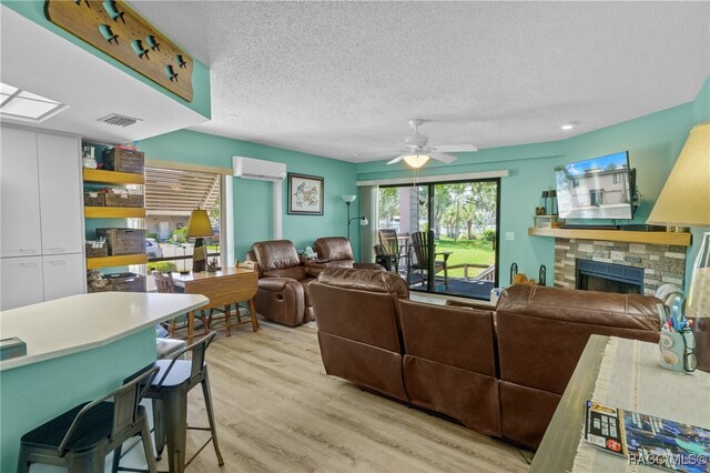 living room featuring a textured ceiling, a wall unit AC, ceiling fan, light hardwood / wood-style floors, and a stone fireplace