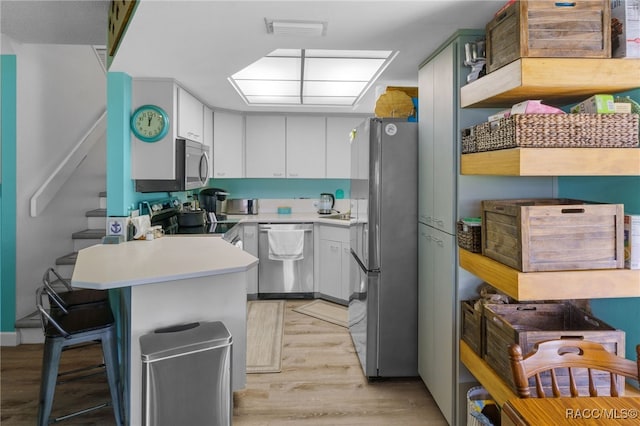 kitchen featuring a kitchen bar, white cabinets, light wood-type flooring, and appliances with stainless steel finishes