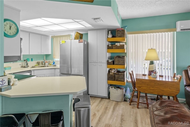 kitchen featuring stainless steel refrigerator, sink, light hardwood / wood-style flooring, a wall unit AC, and white cabinets