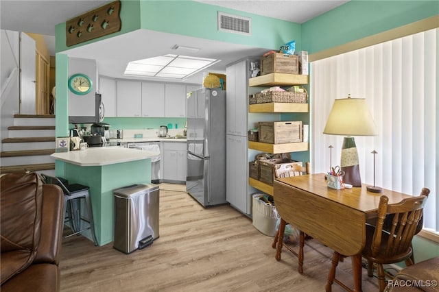 kitchen with backsplash, white cabinets, stainless steel appliances, and light wood-type flooring