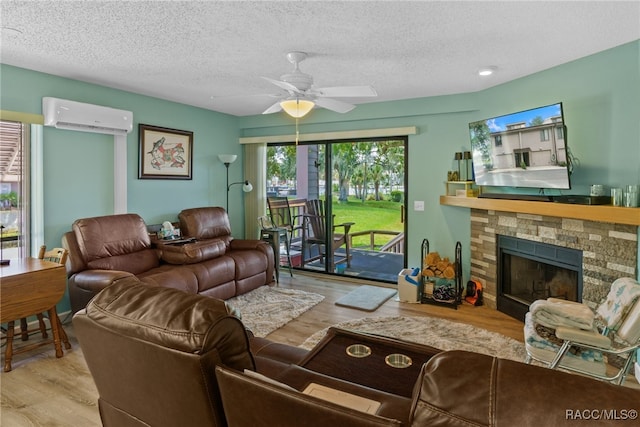 living room featuring a textured ceiling, light hardwood / wood-style floors, an AC wall unit, and ceiling fan