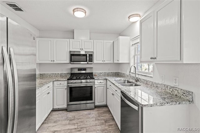 kitchen with stainless steel appliances, light stone countertops, sink, and white cabinets