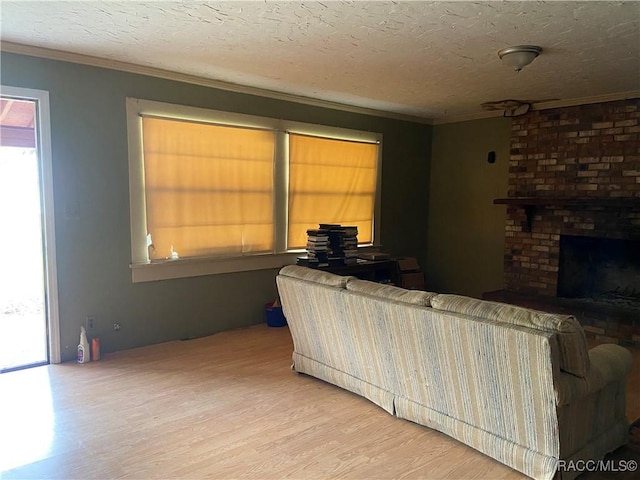 living area featuring light wood finished floors, a brick fireplace, crown molding, and a textured ceiling