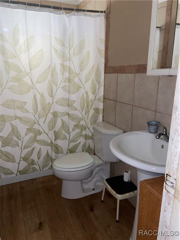 full bathroom featuring toilet, a shower with shower curtain, wood finished floors, and tile walls