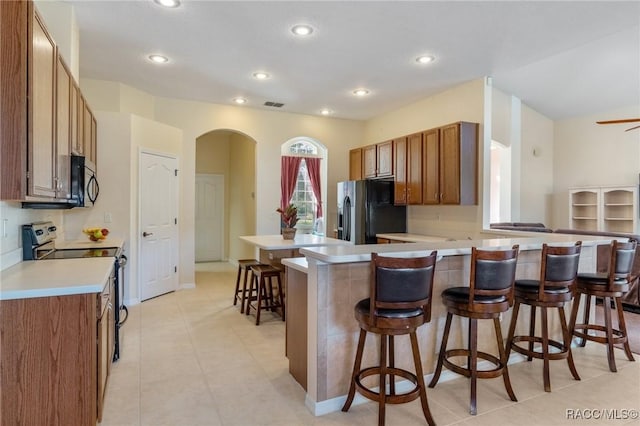 kitchen featuring ceiling fan, a kitchen breakfast bar, kitchen peninsula, light tile patterned flooring, and appliances with stainless steel finishes