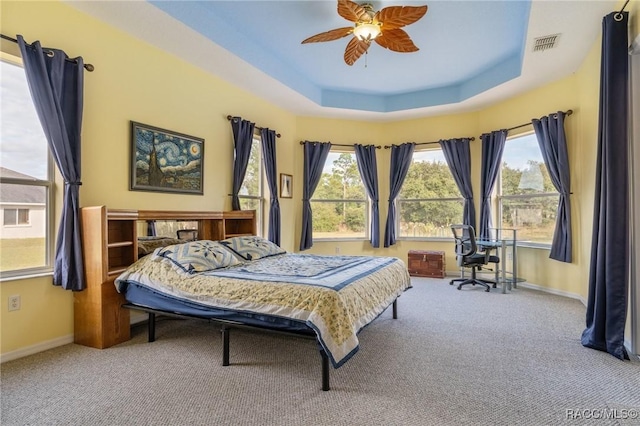 carpeted bedroom featuring a tray ceiling, multiple windows, and ceiling fan