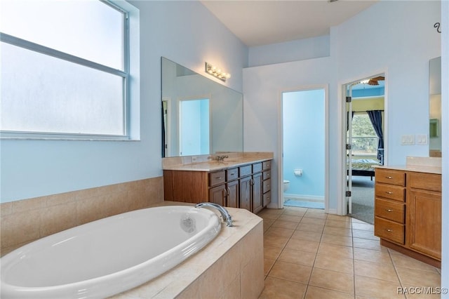 bathroom with tile patterned floors, vanity, a relaxing tiled tub, and toilet