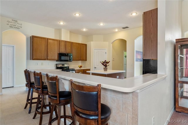 kitchen featuring kitchen peninsula, a breakfast bar, light tile patterned floors, and stainless steel electric range