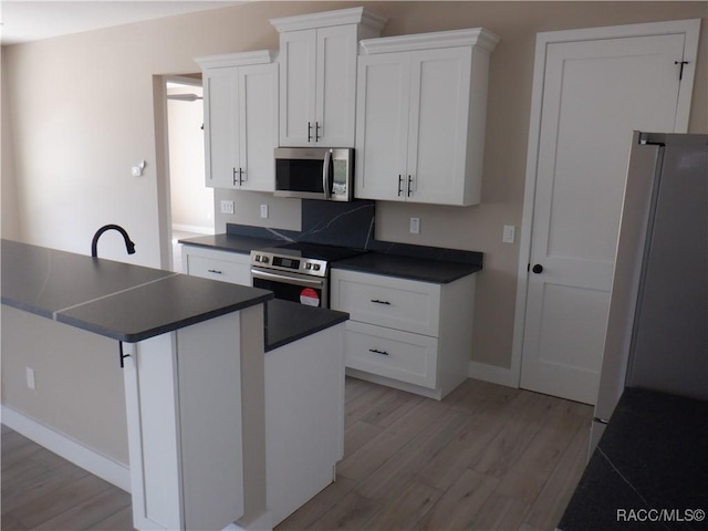 kitchen featuring dark countertops, appliances with stainless steel finishes, white cabinetry, and light wood-type flooring