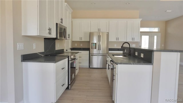 kitchen with dark countertops, white cabinetry, stainless steel appliances, and a sink