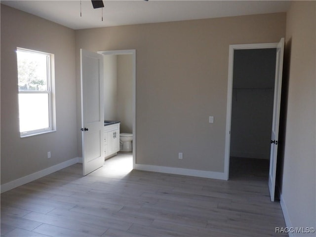 unfurnished bedroom with a walk in closet, baseboards, light wood-style floors, and ensuite bathroom