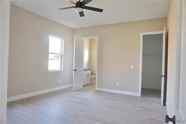 unfurnished bedroom with a spacious closet, baseboards, light wood-style floors, a closet, and ensuite bath