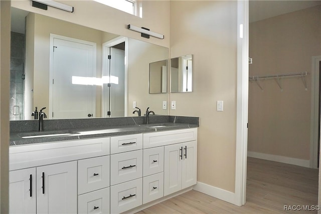 bathroom featuring a sink, baseboards, wood finished floors, and double vanity